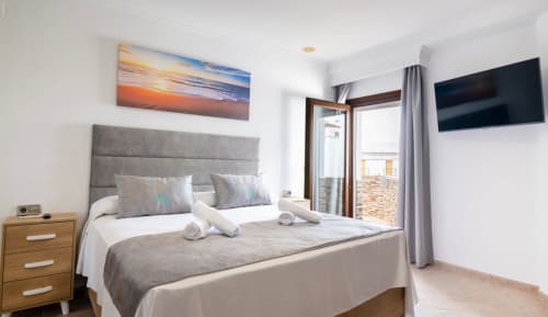 Moderna habitación triple en Boutique Zahara de los Atunes con cabecero gris, acceso a balcón, TV pantalla plana y atardecer
