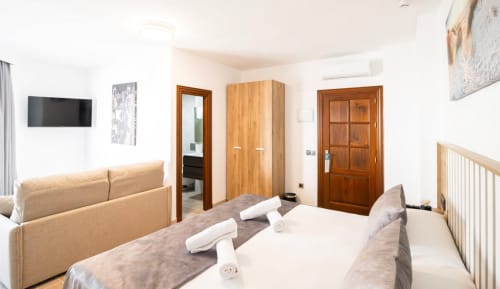 Luminosa habitación triple en Boutique Zahara con cama, sofá, puertas de madera, TV y comodidades modernas