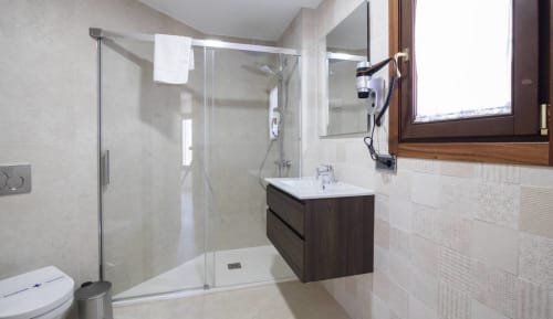 Baño moderno con ducha de cristal, tocador de madera oscura y azulejos blancos en el hotel boutique Zahara de los Atunes de Cádiz