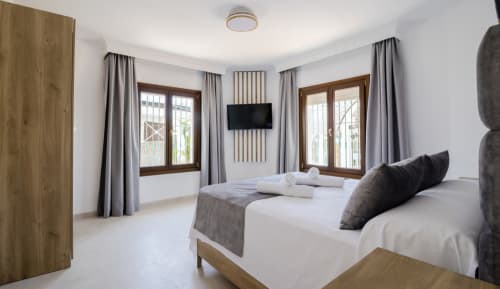 Moderno dormitorio doble en Boutique Zahara de los Atunes con camas individuales, puertas de madera, cortinas grises y TV de pared