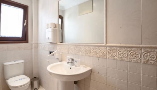 Baño luminoso con lavamanos pedestal, inodoro y cenefa de azulejos decorativos del hotel boutique Zahara de los Atunes en Cádiz