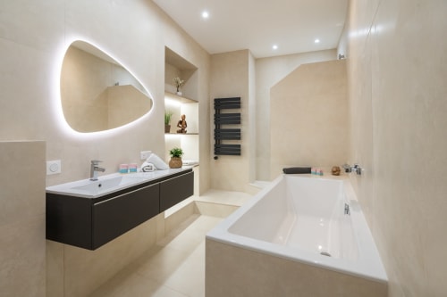 Modern bathroom in Enjoy Nice's Zen apartment #4 featuring illuminated oval mirror, black vanity, and sleek white bathtub in