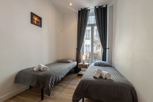 Twin bedroom at Enjoy Nice apartment in Nice with dark striped bedding, rolled towels, and Parisian balcony view