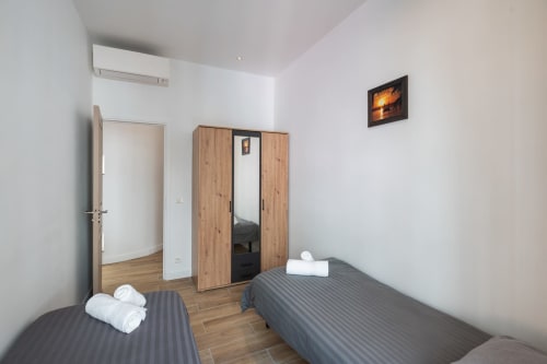 Zen apartment at Enjoy Nice hotel in Nice featuring twin beds with white towels, wooden wardrobe, AC unit, and wooden
