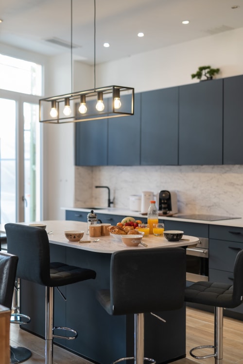 Modern kitchen in Enjoy Nice's Zen apartment featuring blue cabinetry, marble countertop, and pendant lighting with breakfast
