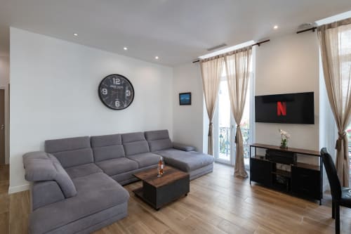 Modern Zen apartment at Enjoy Nice with gray sectional sofa, wall-mounted TV, wooden furniture, and French balcony access