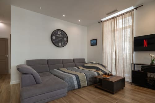 Modern Zen apartment at Enjoy Nice featuring gray sectional sofa, wall clock, flat-screen TV, and elegant sheer curtains.