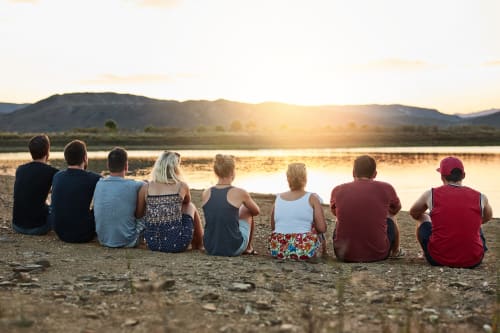 Groupe d'invités assis sur la plage de sable au coucher du soleil, surplombant une eau calme avec les montagnes, Domaine Alga Bourg-Charente