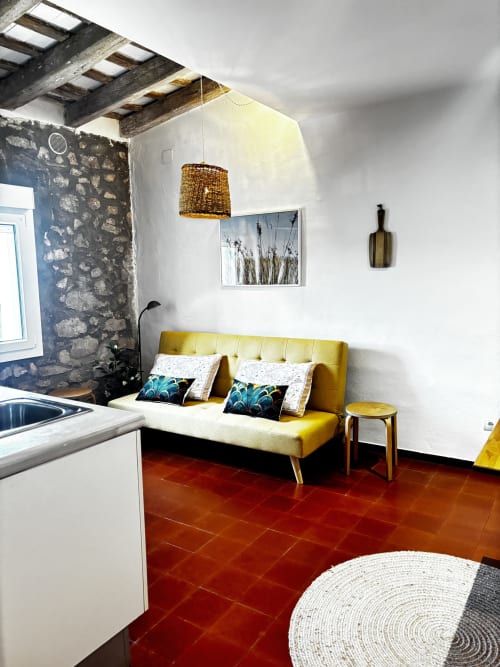 Bright apartment at Mas Ribas Hotel in Palamós with mustard sofa, exposed beams, stone wall, and terracotta floors