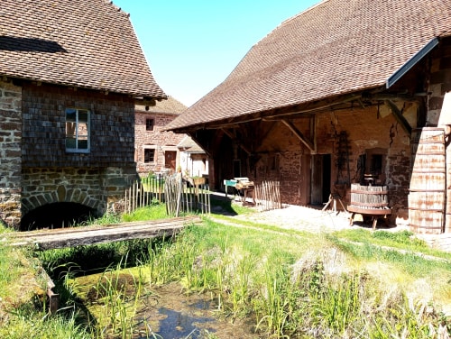 Cour du gîte Paulusmühle à Soucht en France avec bâtisses historiques en pierre, toitures carrelées et petit bassin