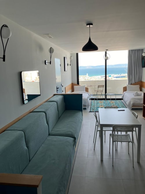 Séjour moderne à Tanger avec vue sur mer, canapé turquoise, deux lits, table à manger et paysage côtier méditerranéen