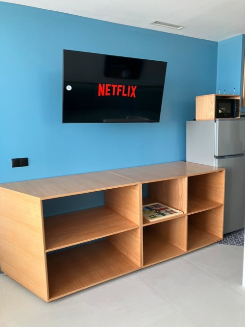 Séjour moderne avec murs bleus, téléviseur affichant Netflix, étagères en bois et kitchenette