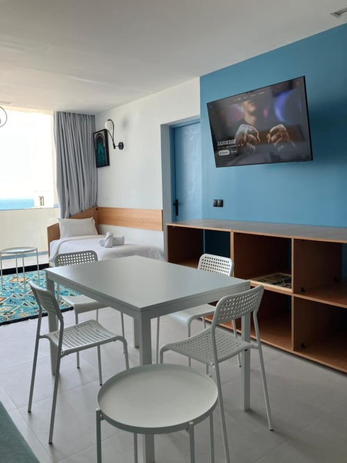 Coin repas moderne d'un appartement avec vue sur mer à Tanger, table blanche, mur bleu, TV et lit en arrière-plan