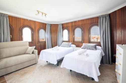 Espaciosa habitación cuádruple en Boutique Zahara de los Atunes con dos camas, sofá, paredes de madera y ventanas arqueadas con vistas a Cádiz
