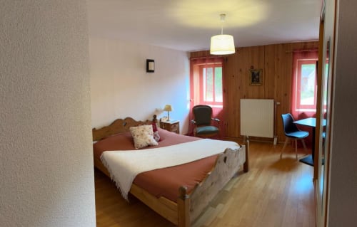 Chambre fleurie à l'Auberge Du Ruxelier, Chenimenil : lit en bois avec vue sur le jardin, luminaire suspendu, lambris bois.