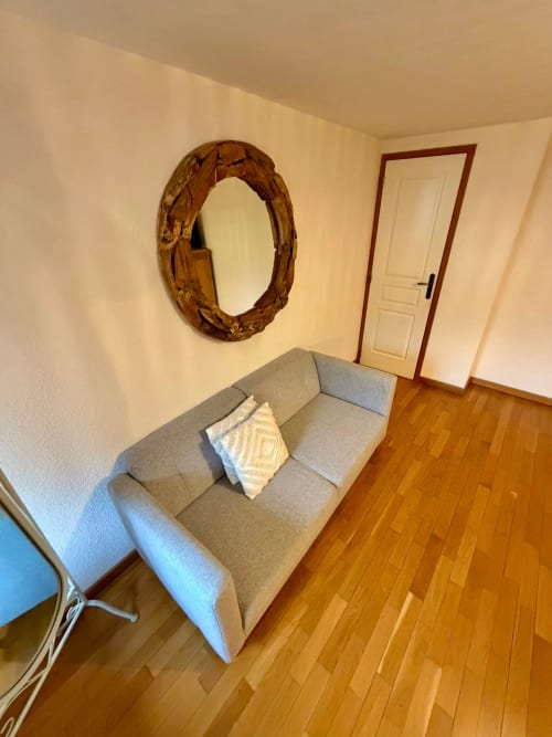 Fauteuil gris avec coussin dans la chambre Ancolie de l'Auberge Du Ruxelier à Chéniménil, avec miroir en bois et parquet