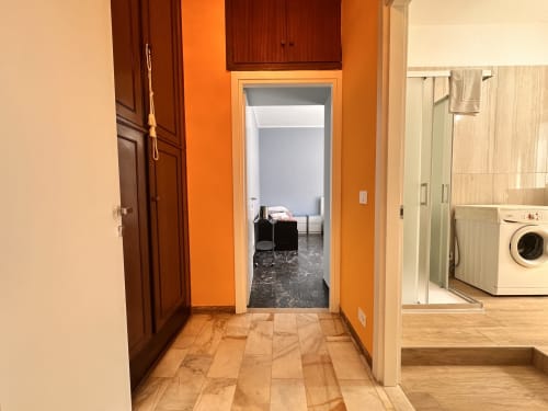 Corridoio con pareti arancioni che conduce alla camera da letto in La Fenice Studio Flat, Finale Ligure, con lavanderia visibile sulla destra
