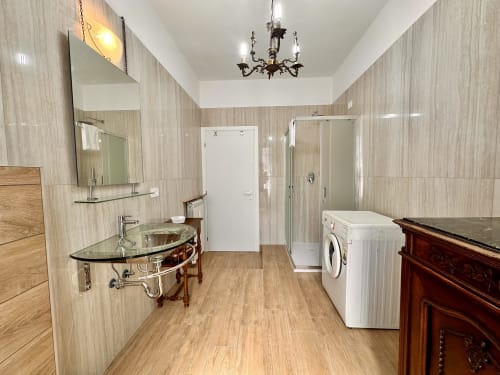 Bagno moderno nel monolocale La Fenice a Finale Ligure, con lavabo in vetro, doccia, lavatrice e piastrelle effetto legno