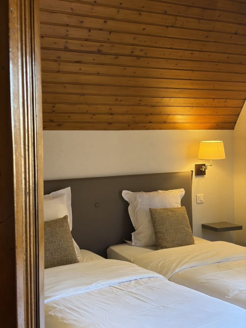 Chambre twin à l'Hôtel de l'Ange à Niedermorschwihr avec plafond en bois, tête de lit foncée et éclairage chaleureux