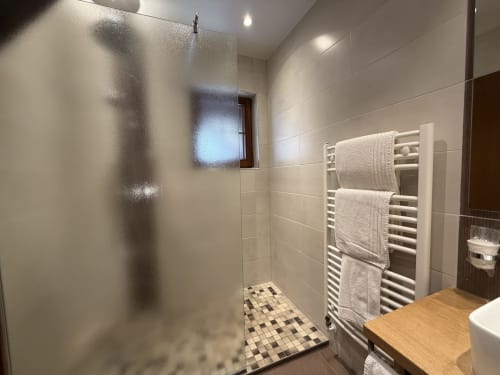Salle de bain moderne de l'Hôtel de l'Ange avec douche à l'italienne, paroi en verre dépoli, sèche-serviettes chauffant et carrelage géométrique