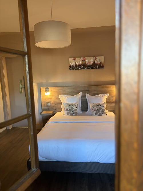 Chambre d'hôtel moderne à l'Hôtel de l'Ange avec lit queen, tête de lit en bois, lampe suspendue et art floral mural