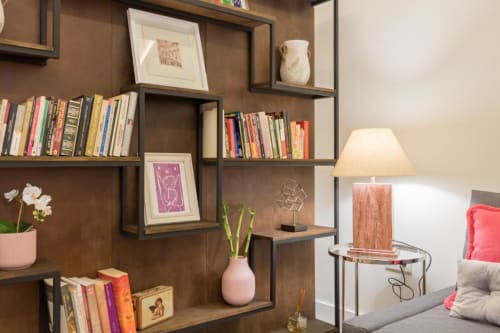 Habitación Almirante B de Calma Places en Sevilla con estanterías de madera, libros, objetos decorativos, lámpara de mesa y vistas de la ciudad