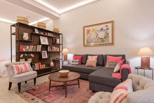 Sala moderna de Calma Places Sevilla con sofá gris, butaca beige, estantería de madera y cojines coloridos
