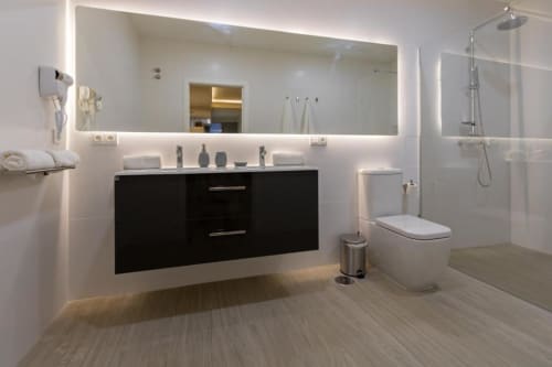 Baño moderno en Calma Places Sevilla con espejo iluminado, mueble negro, ducha de efecto lluvia y piso de madera clara