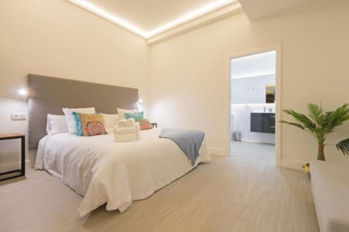 Dormitorio moderno en Calma Places Sevilla con vistas a la ciudad, ropa de cama crema, suelos de madera y mobiliario contemporáneo