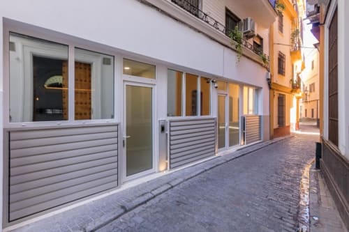Moderna fachada del hotel Calma Places en Sevilla con puertas de cristal y aluminio blanco en calle histórica adoquinada
