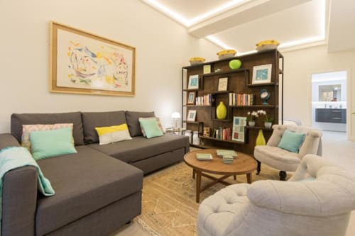 Sala de estar moderna en Calma Places Sevilla con sofá oscuro, estanterías de madera, detalles turquesa y decoración contemporánea