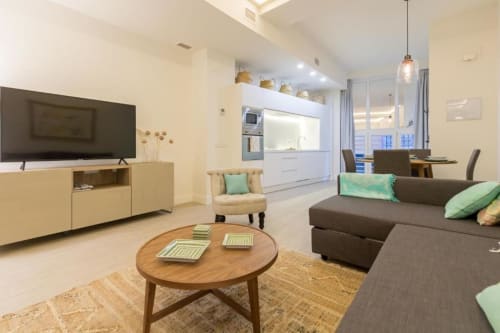 Moderna sala de estar en Calma Places Sevilla con sofá gris, mesa de café de madera y vistas de la ciudad