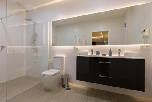 Baño moderno en Calma Places Sevilla con ducha de acceso directo, tocador negro, espejo retroiluminado e iluminación de piso con calefacción