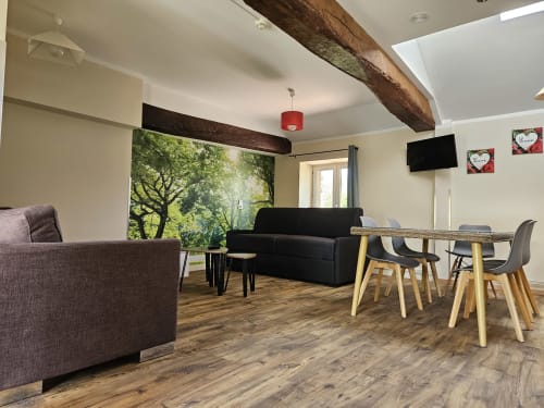 Séjour moderne aux Gîtes Les Muriers avec fauteuil violet, canapé noir, table à manger, poutres bois et œuvre d'art vue jardin