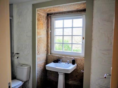 Banheiro rústico com lavatório de pedestal, sanitário e janela com vista para o jardim na quinta Quinta da Coutada em Portugal