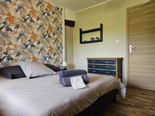 Chambre aux Gîtes Les Muriers avec papier peint fleuri, literie blanche, commode bleue et équipements modernes à Bourgvilain