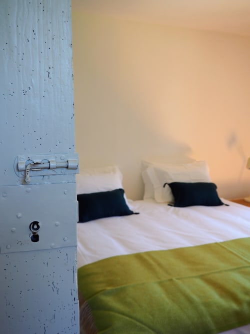 Quarto acolhedor na Quinta da Coutada com parede de concreto branco, roupa de cama verde, almofadas pretas e iluminação ambiente quente em Arcos