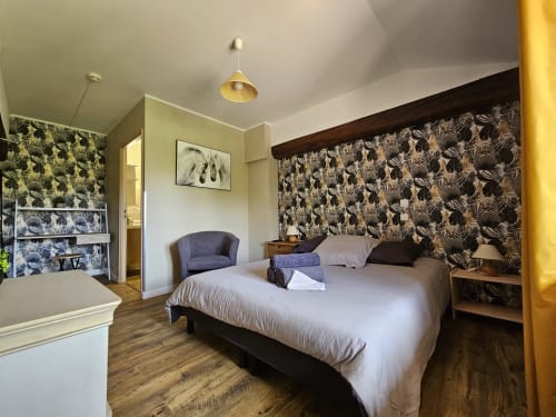 Chambre aux Gîtes Les Muriers avec lit queen-size, tête de lit à motifs, fauteuil et pilier jaune