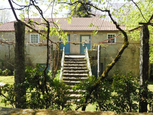 Cottage de pedra com portas azuis na Quinta da Coutada cercado por jardim verde e vinhas trepadeiras em Arcos de Valdevez