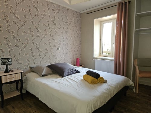 Chambre lumineuse aux Gîtes Les Muriers avec papier peint fleuri, lit blanc, vue jardin et serviettes jaunes à Bourgvilain