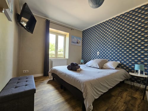Chambre moderne aux Gîtes Les Muriers avec mur d'accent motifs, lit queen-size, téléviseur, vue sur le jardin et parquet