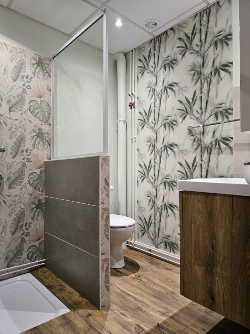 Salle de bain moderne aux Gîtes Les Muriers avec papier peint botanique, meuble lavabo en bois, douche italienne et sol aspect bois