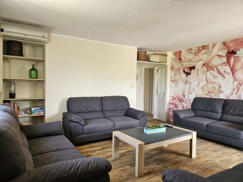 Séjour moderne du Gîte Le Tilleul avec canapés sombres, table en bois et papier peint floral rose à Bourgvilain