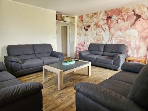 Salon moderne avec canapés noirs, table basse en bois et papier peint fleuri aux Gîtes Les Muriers, Bourgvilain
