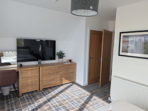 Modern bedroom at Flotnar Hus B&B in Keiss with wooden dresser, TV, and tartan flooring
