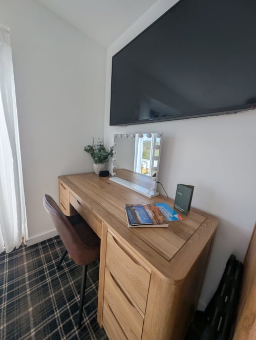 Modern workspace at Flotnar Hus B&B with wooden desk, mounted TV, illuminated mirror, and potted plant in Keiss