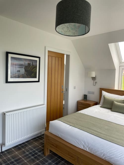 Modern bedroom at Flotnar Hus B&B in Keiss with wooden bed, grey pendant light, and framed landscape artwork
