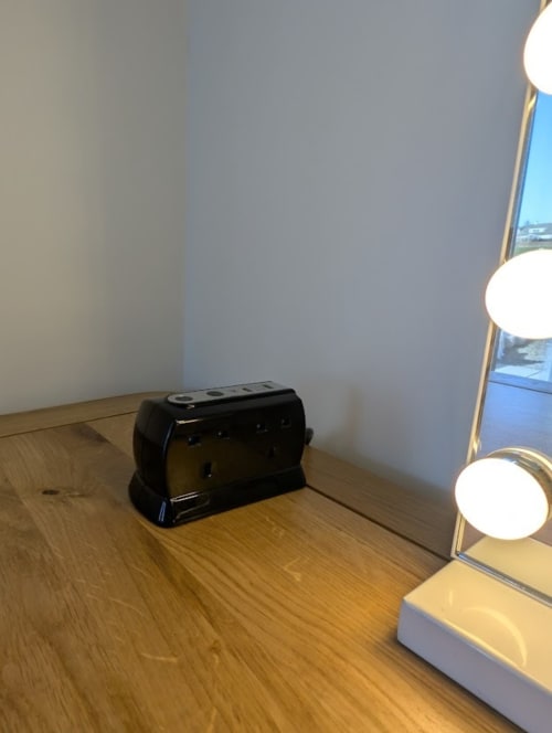 Black toaster on wooden floor next to white vanity with lights in Flotnar Hus sea view room, Keiss