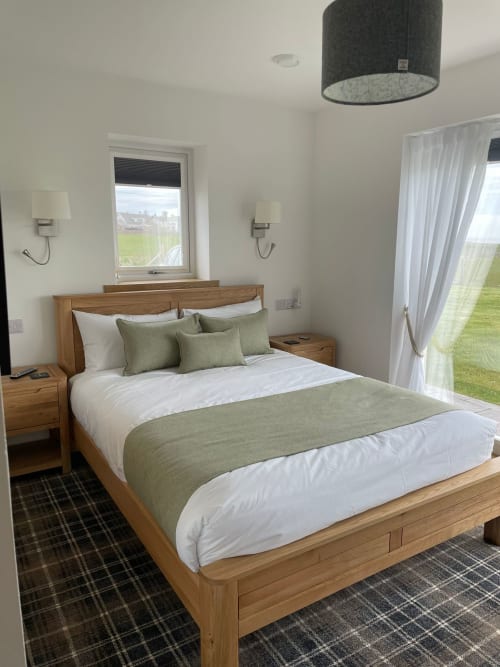 Modern bedroom at Flotnar Hus with wooden bed, green and white bedding, sea views through windows, and contemporary