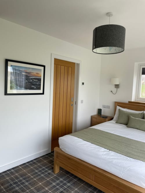 Modern bedroom at Flotnar Hus B&B in Keiss with wooden bed, green bedding, pendant light, and framed sea view artwork